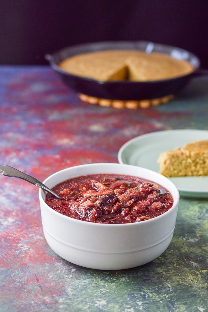 The sauce made of figs in a white bowl with some skillet of cornbread in the background