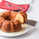 A cake server with a piece of cake on it held over the rest of the cake - square