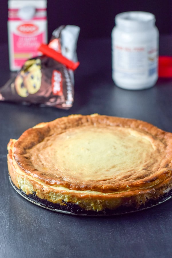 Cheese cake out of the oven and sides taken off with chocolate chips, cream and fluff in the background