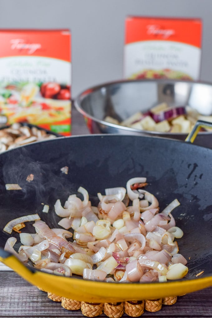 Shallots sautéed in a wok and cut up eggplant in the background