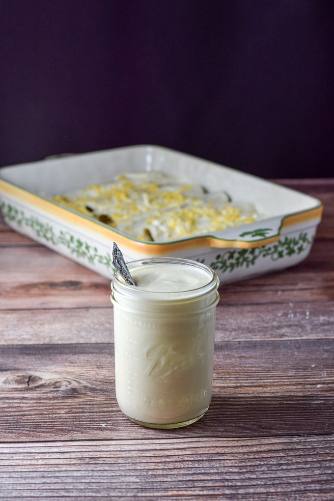 Vertical view of the sour cream sauce in front of a pan full of chicken enchiladas