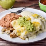 Guacamole and more sour cream sauce draped over the enchiladas with beans on the plate as well