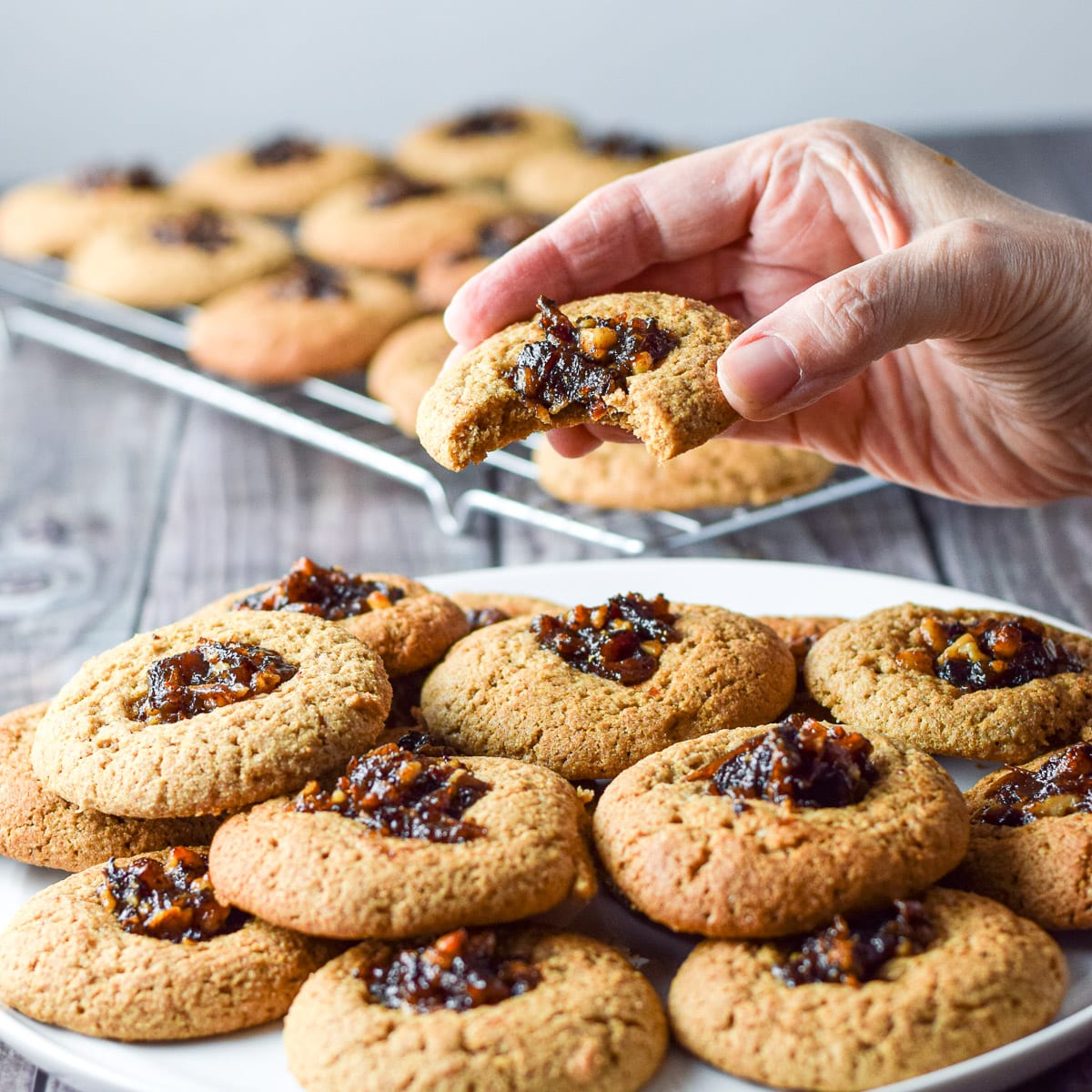 Close up of a white plate with one of the muffins with a bite taken out of it. There are more muffins in the background on a rack - square