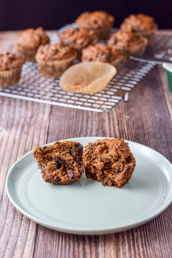 One of the muffins broken in half and on a green plate with the muffins on a wire rack in the background