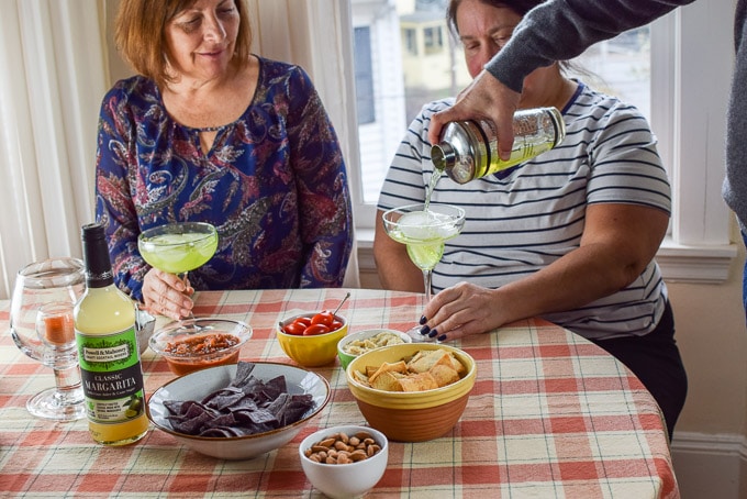 A male pouring the margaritas in the glasses so everyone can party. Lots of apps on the table
