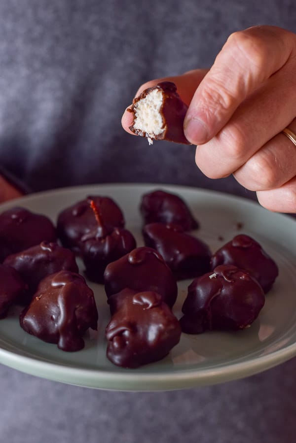 Close up of a hand holding a chocolate coconut ball with a big bite taken out of it