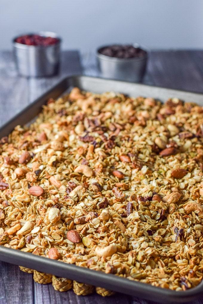 The granola baked and cooling on the table with some chocolate chips and cranberries in the background.