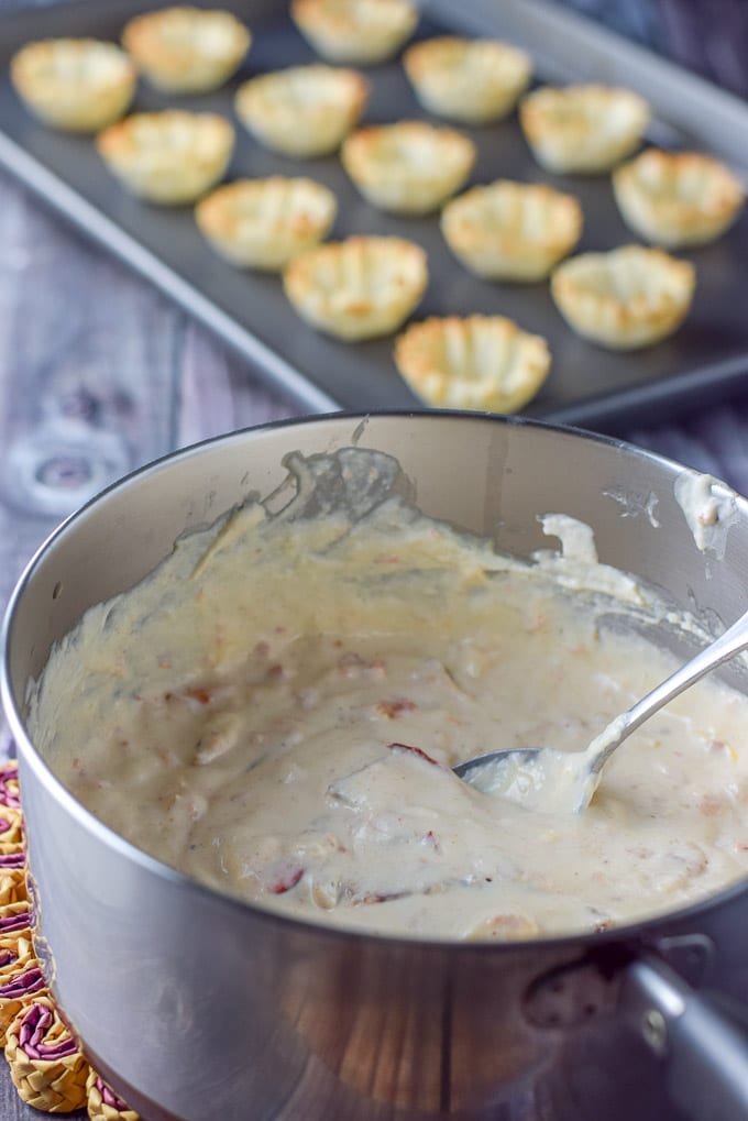 Cooked and melted cream cheese with all the condiments and lobster in a pan with the phyllo tarts in the background