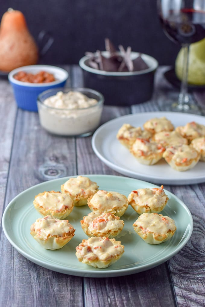 Cooked lobster filled phyllo cups on a few plates with more appetizers in the back