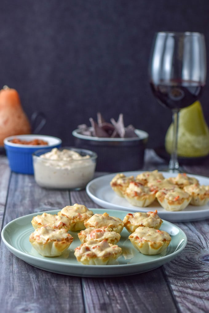 A green plate with phyllo cups filled with the lobster and cream cheese with more dip in the back and a glass of wine