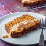 A green plate with a piece of pumpkin bread on it with a wire rack in the background - square