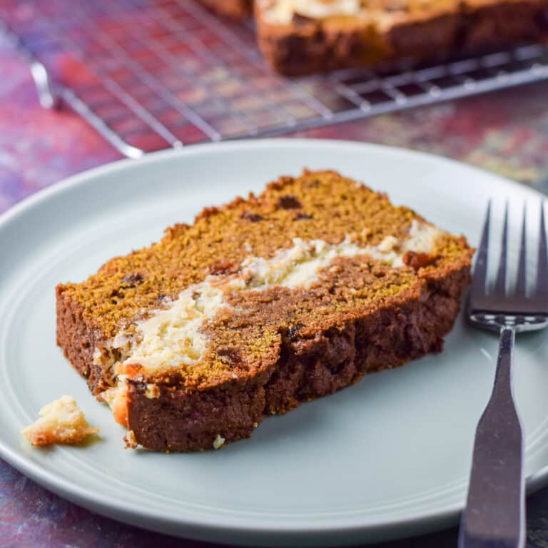 A green plate with a piece of pumpkin bread on it with a wire rack in the background - square