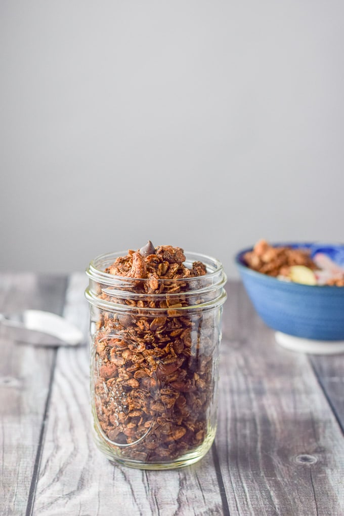 A pile of granola in a ball jar with a scoop and bowl in the background