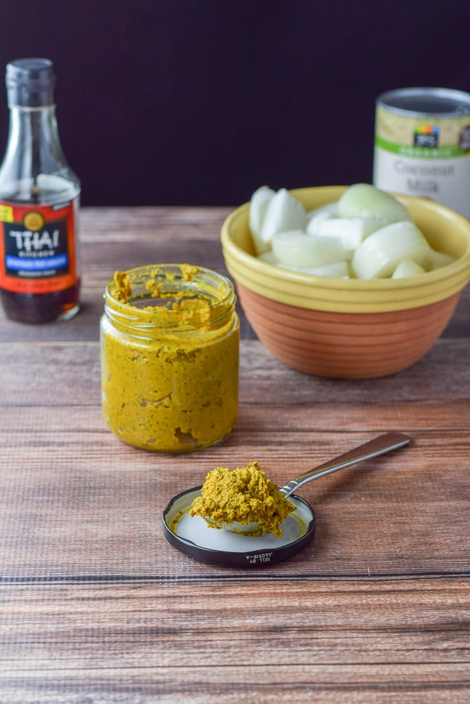 Curry on a spoon with chopped onions, fish sauce and coconut milk in the background
