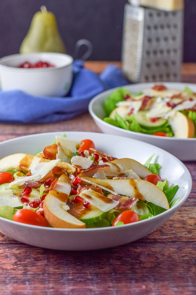 Balsamic dressing and shaved parmesan on the salad with another salad and cheese in the background