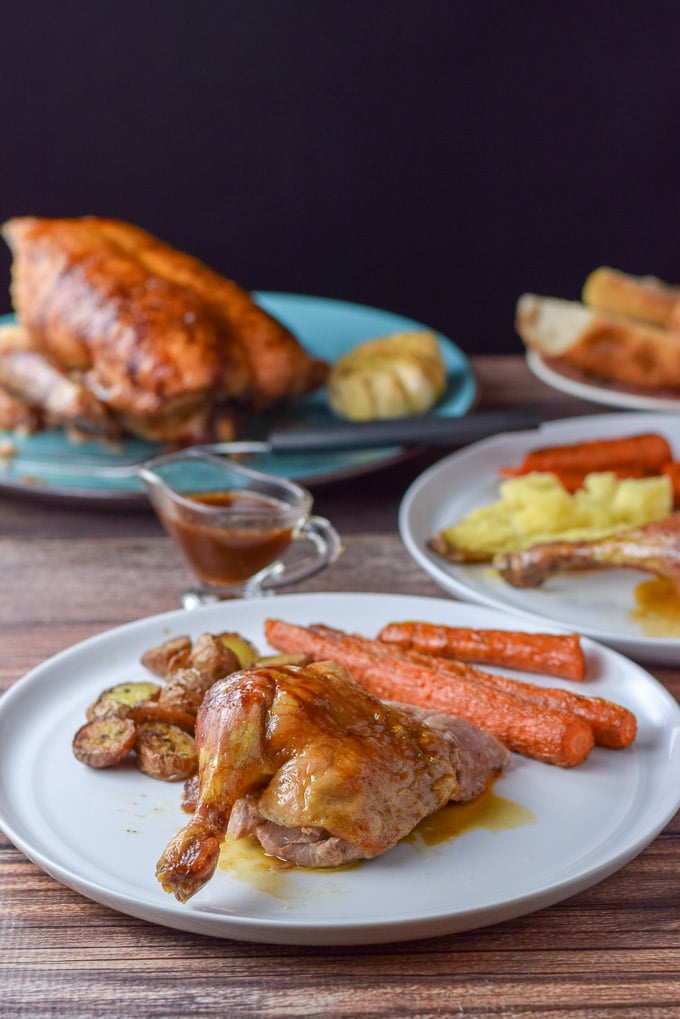 Plated leg quarter of the duck with roasted carrots and potatoes on a plate with the duck in the background