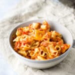 A grey bowl of bacon tomato pasta on a beige napkin - square