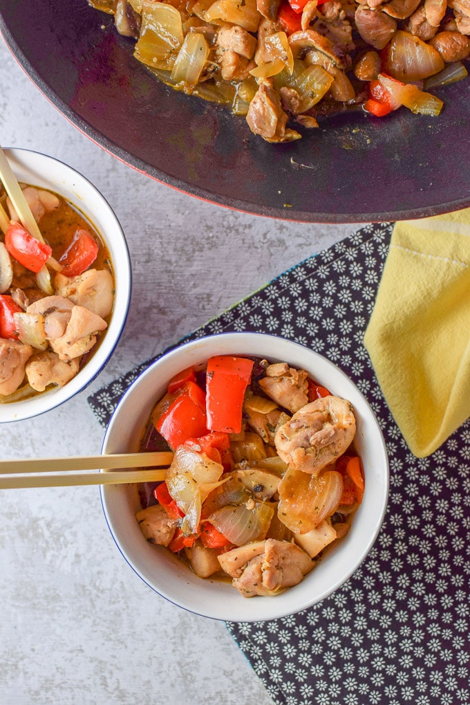 Overhead shot of the stir fry with chicken in two bowls with a wok in the back filled with the dish