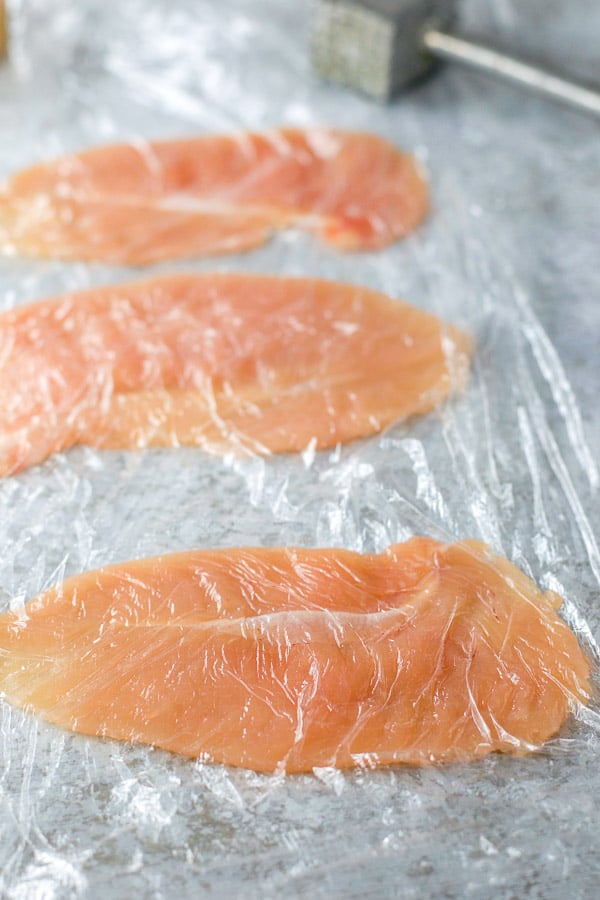 Chicken tenders pounded flat between two plastic wrap sheets