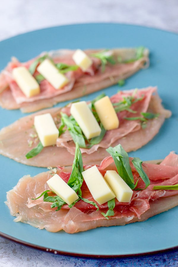 Three pounded chicken tenders with prosciutto, tarragon and cheese on a blue plate