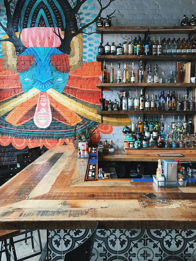 Half of a bar with bottles on shelves and a colorful painting on the wall