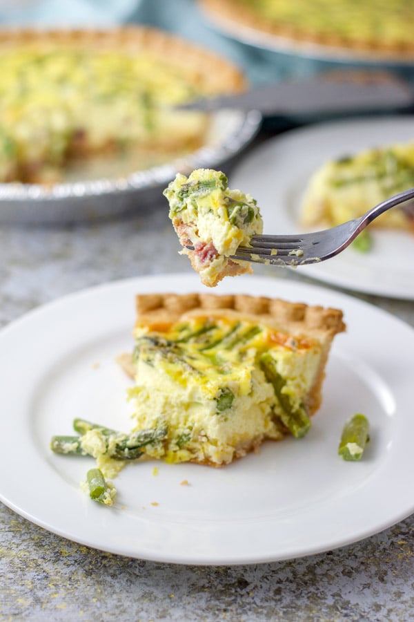 A forkful of th quiche held over the plate with the two quiches in the background