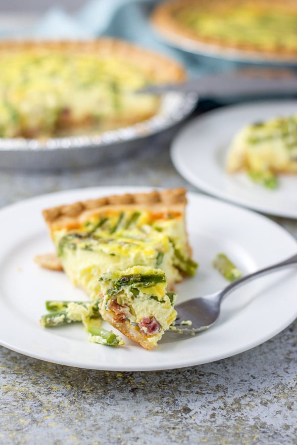 The fork with a piece of quiche on the front of the plate with the two quiches in the background