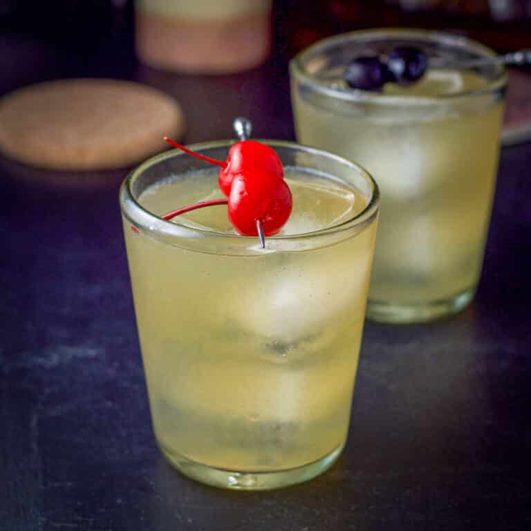 Two glasses of the whiskey sour, red cherries in front, dark in back - square