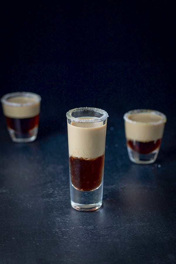 Near vertical view of the tall shot glass filled with jelly shot ingredients. There are two shot glasses behind it
