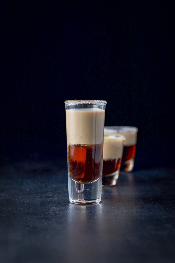 A line up of the donut shot, tall glass with two little shot glasses behind it