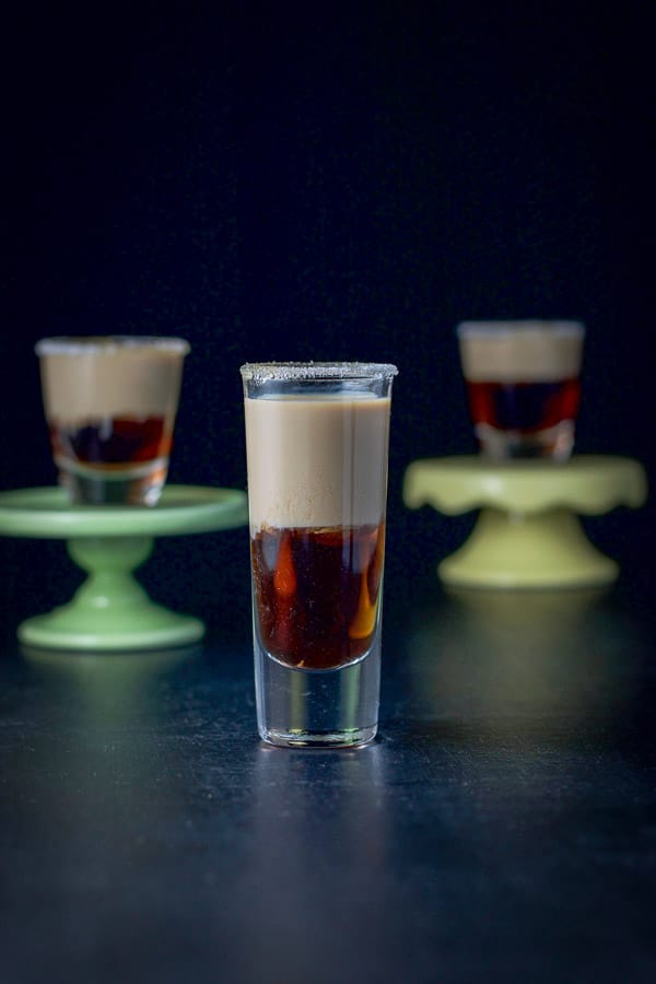 Tall glass of donut shot in front with two short glasses on little pedestals 