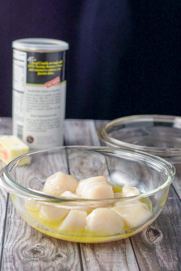 Sea scallops in a casserole dish with melted butter on top with more butter and breadcrumbs