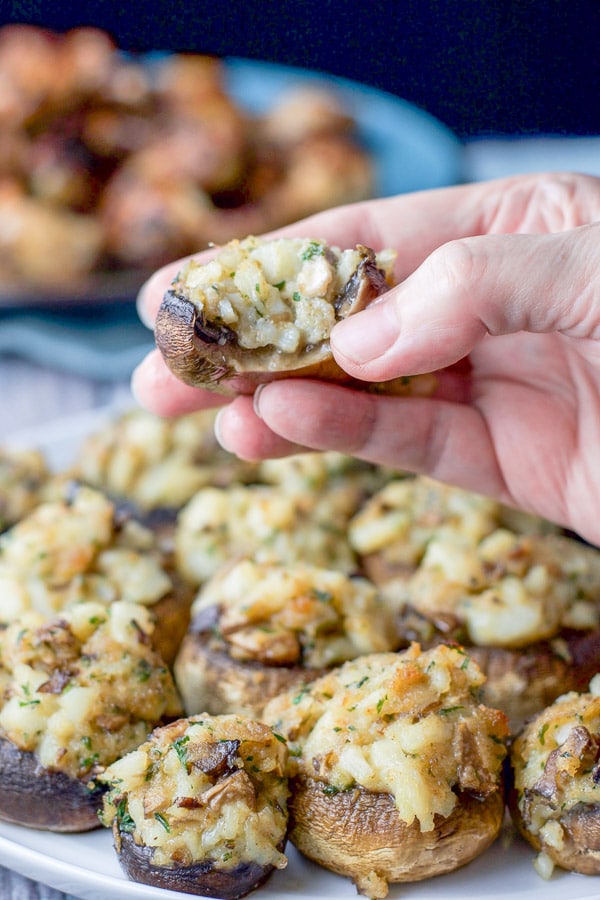 My hand holding one of the stuffed mushrooms over the big plate of them
