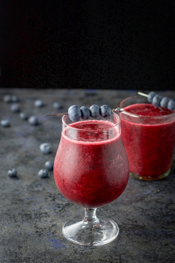 A tulip and double old fashioned glass with the daiquiri in it along with a martini pick with blueberries on it