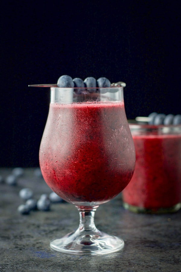 Vertical view of the daiquiri in a tulip glass and another glass behind it along with blueberries on the table