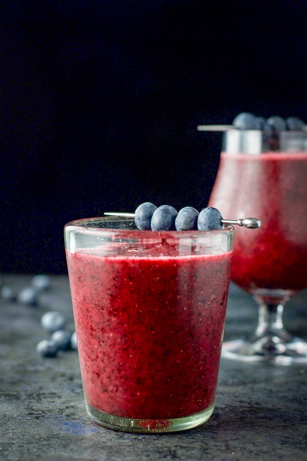 vertical view of the double old fashioned glass in front of the tulip glass with the daiquiri and blueberries on picks