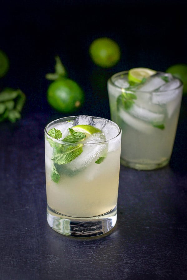 Two glasses of the mojito with limes and mint in the background