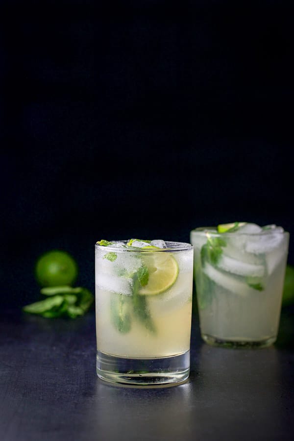 Vertical view of the the shorter glass in front of the larger. They are filled with the mojito with lime and mint floating in the glass