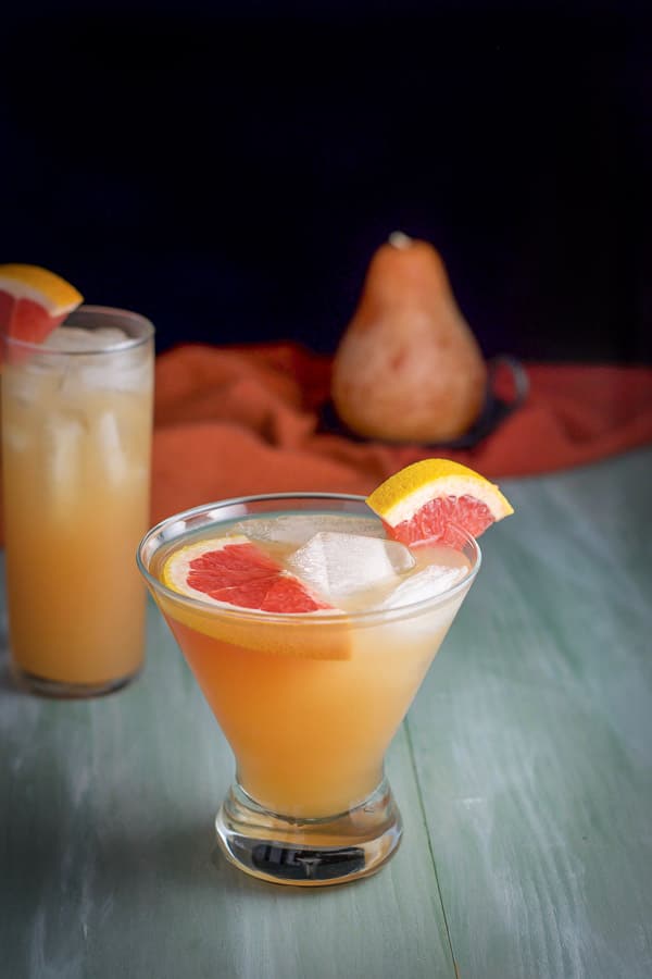 Short martini glass in front of the collins glass both filled with the Frenchie with a few slices of grapefruit in them