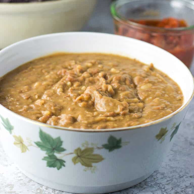 A bowl filled with creamy pinto refried beans with some salsa in the background - square