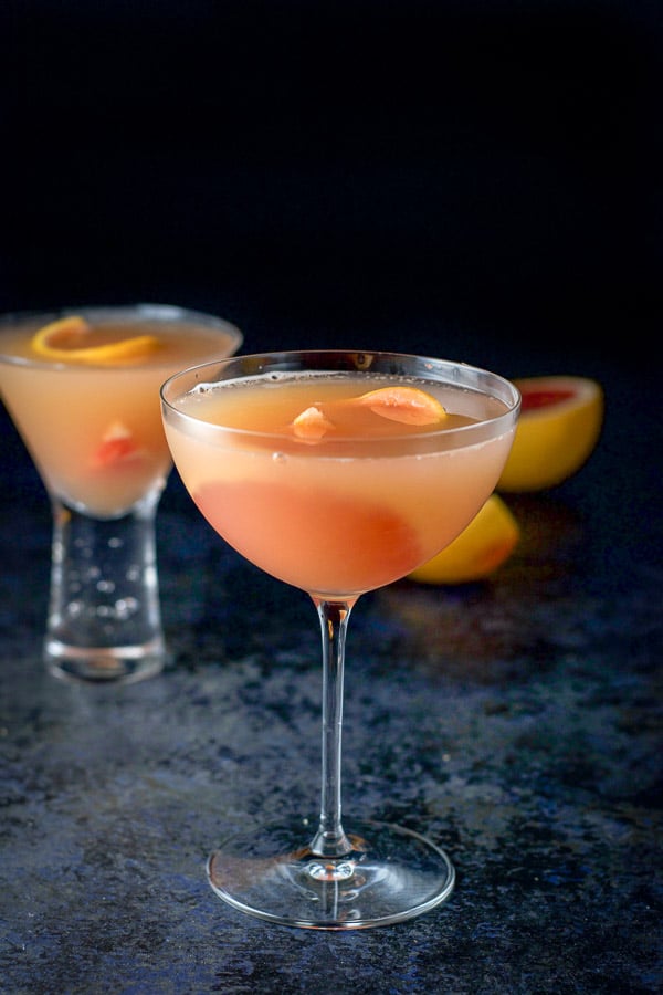 A bowl shaped glass of the cosmo in front with a bubble glass of in the background