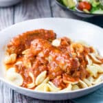 A sausage and sauce on pasta in a white plate - square