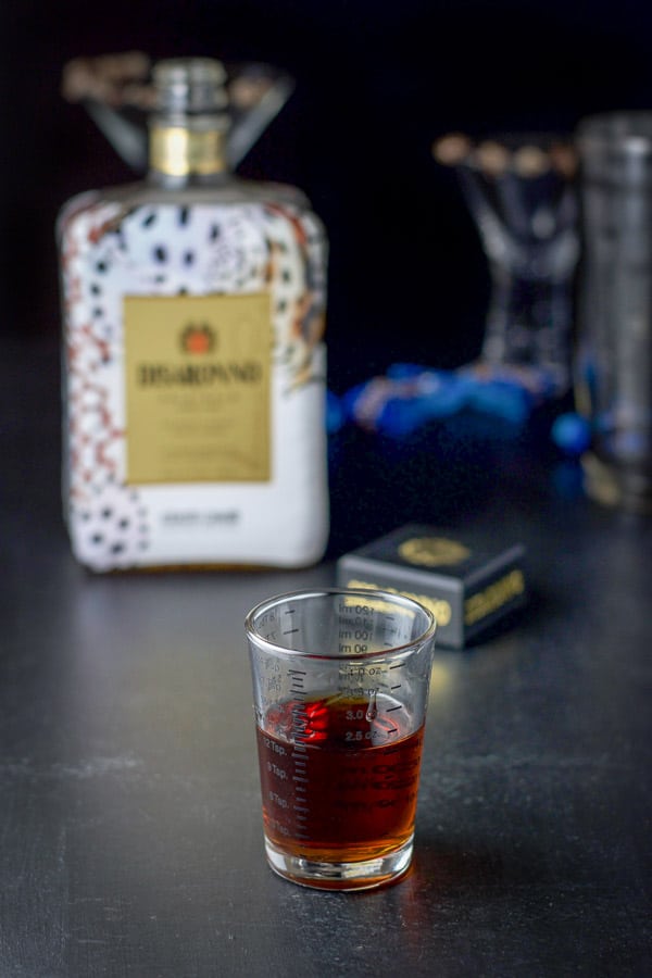 Amaretto measured out with the bottle, garnished glasses and shaker in the background