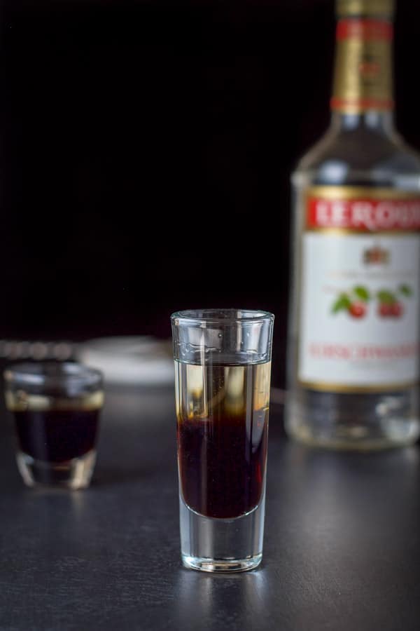 Cherry brandy layered into the glasses with the bottle and spoon in the background
