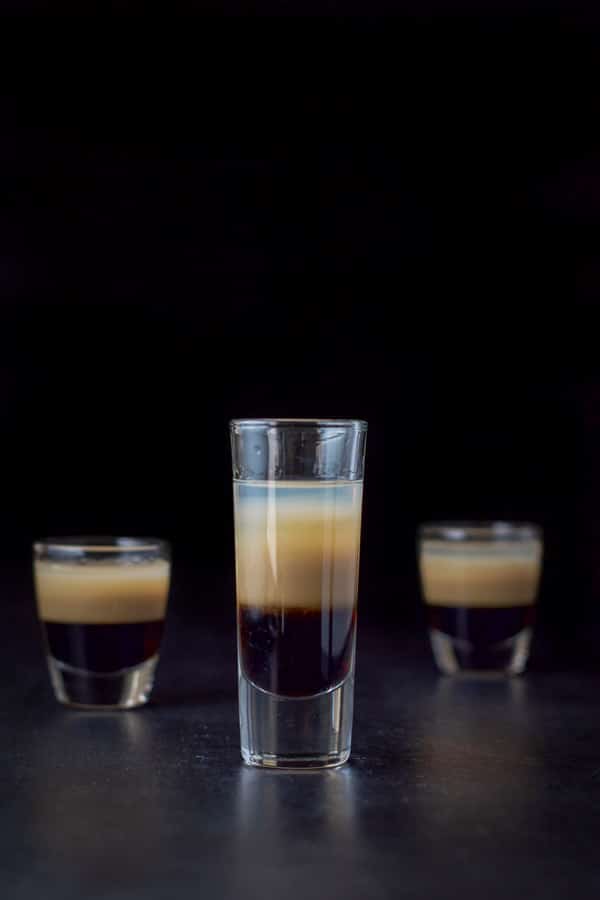 Vertical view of the tall glass filled with the peppermint shot with two other glasses behind it