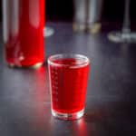 Cranberry vodka in a measuring glass with the bottle behind it