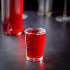 Cranberry vodka in a measuring glass with the bottle behind it