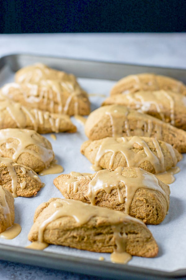 A jelly roll pan covered with parchment paper with a bunch of glazed scones on it
