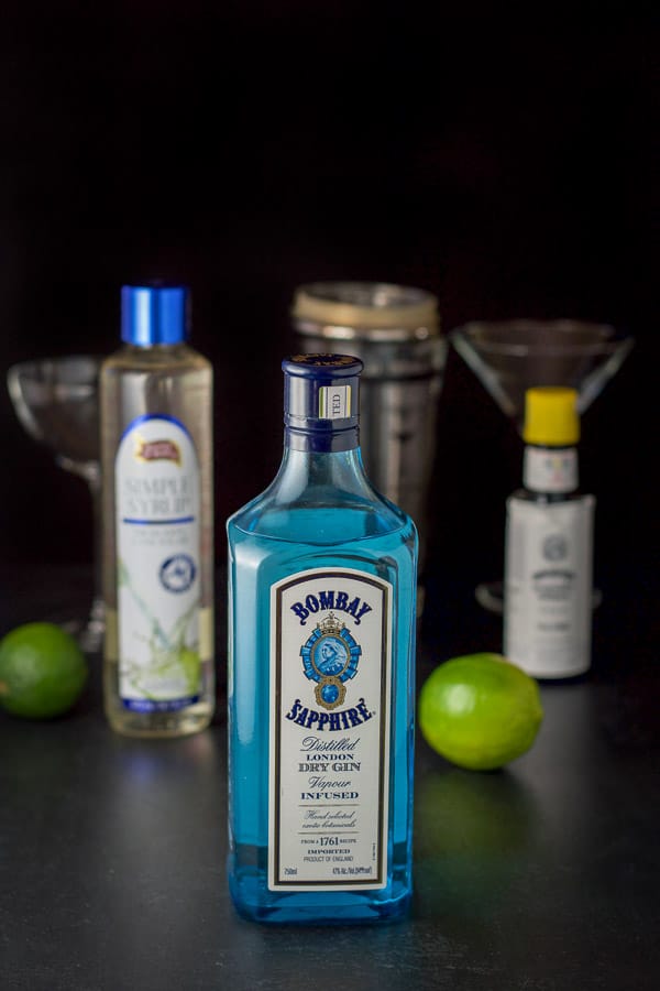 Gin, simple syrup, limes and bitters on the table with the shaker and glassware