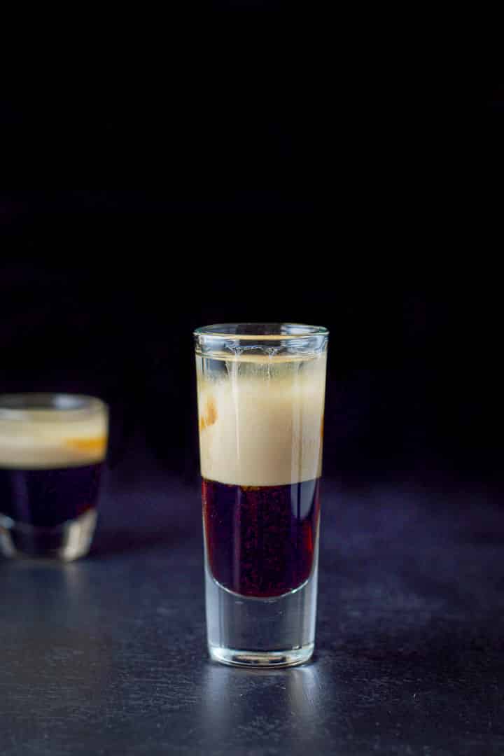 Two glasses filled with the layered shot, the tall glass in front of the shorter glass